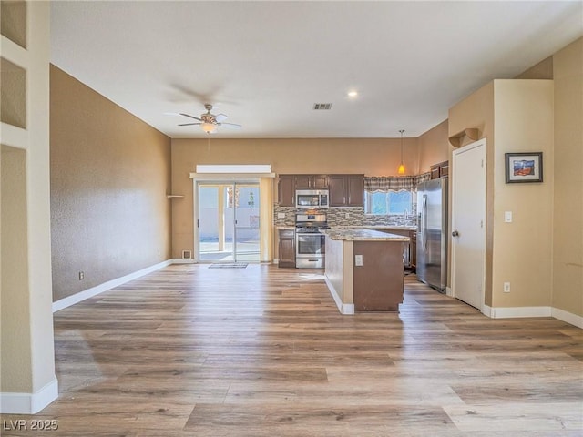 kitchen with a kitchen island, open floor plan, appliances with stainless steel finishes, light wood finished floors, and decorative backsplash