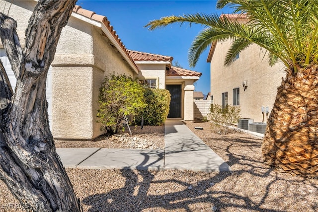 property entrance with stucco siding, a tile roof, and fence