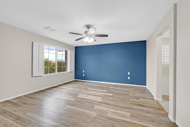 spare room featuring a ceiling fan, light wood-style floors, visible vents, and baseboards