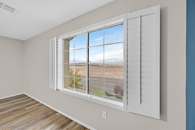 spare room featuring wood finished floors, visible vents, and baseboards