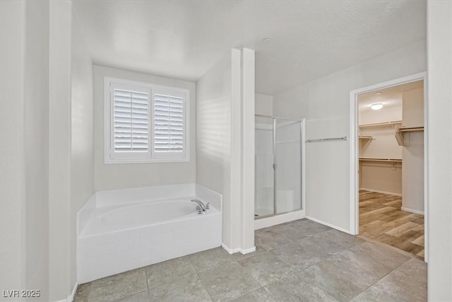 bathroom featuring baseboards, a garden tub, a stall shower, and a spacious closet