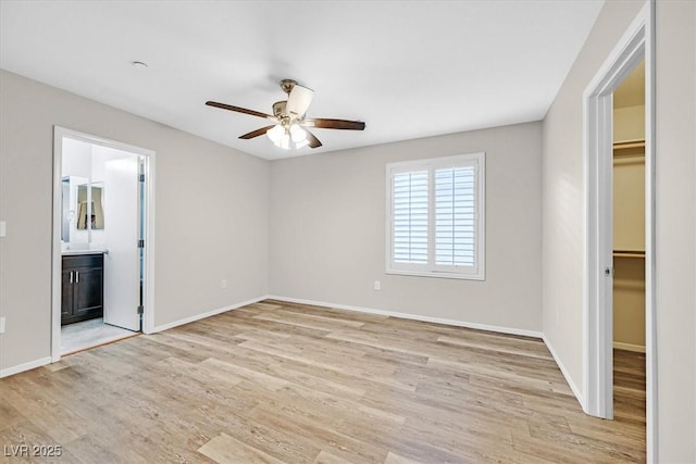 unfurnished bedroom featuring a spacious closet, connected bathroom, baseboards, light wood-style flooring, and a closet