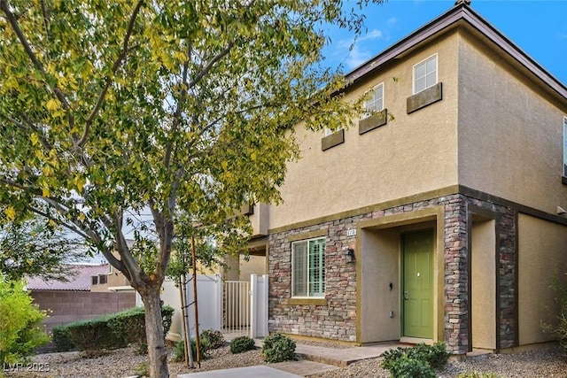 view of front of house featuring stone siding, stucco siding, and fence