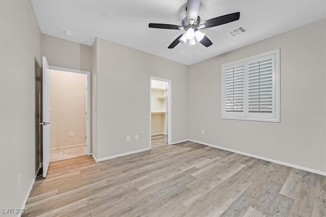 unfurnished bedroom featuring visible vents, light wood finished floors, baseboards, ceiling fan, and a spacious closet