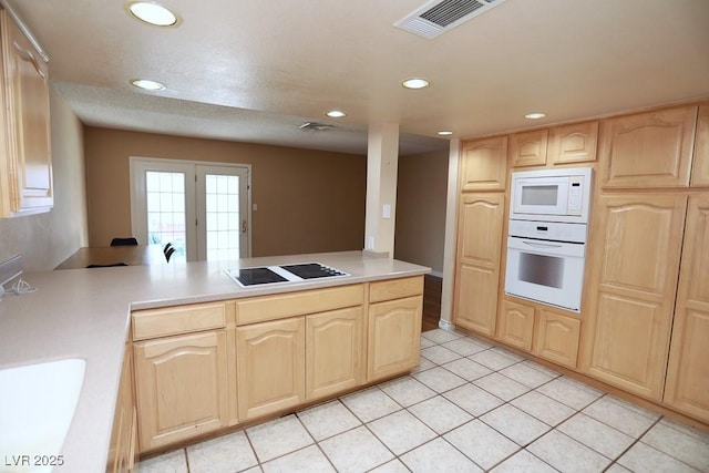 kitchen with visible vents, light brown cabinetry, white appliances, a peninsula, and light countertops