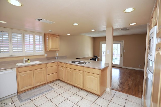 kitchen with light brown cabinetry, visible vents, a sink, and white dishwasher