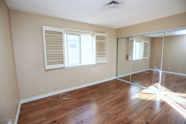 unfurnished bedroom featuring visible vents, baseboards, a closet, and hardwood / wood-style floors