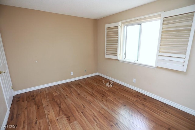 spare room with baseboards and wood finished floors