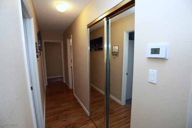 corridor with baseboards, a textured ceiling, and wood finished floors