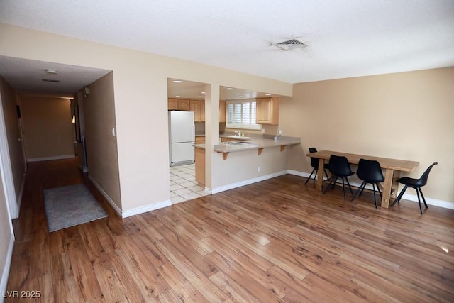 kitchen with visible vents, a breakfast bar area, light countertops, light wood-style flooring, and freestanding refrigerator