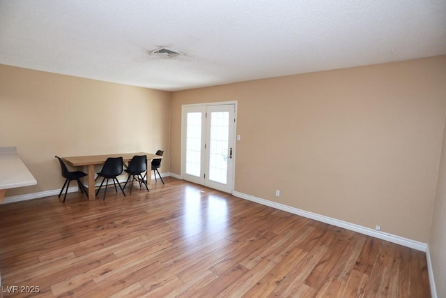 dining area with visible vents, light wood-style flooring, a textured ceiling, and baseboards