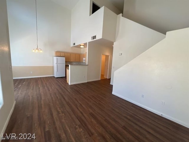 unfurnished living room with baseboards, visible vents, an inviting chandelier, dark wood-style flooring, and a towering ceiling