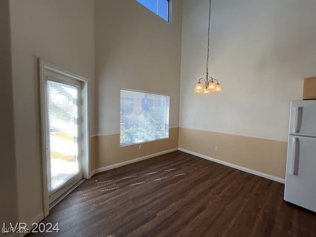 unfurnished dining area with an inviting chandelier, baseboards, dark wood-type flooring, and a high ceiling