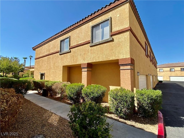 view of property exterior with a tiled roof, an attached garage, and stucco siding