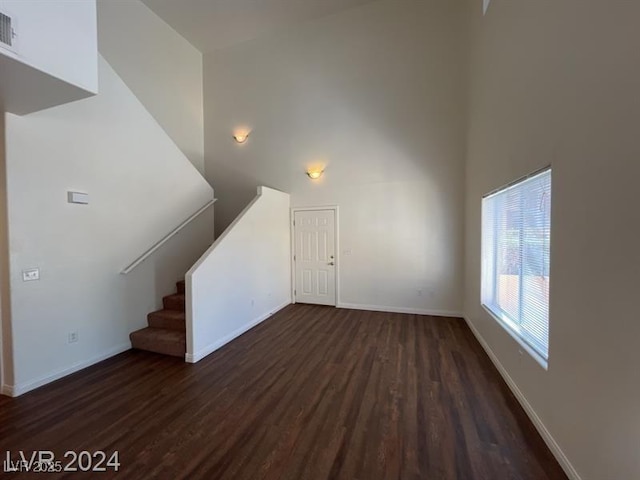 unfurnished living room featuring stairway, dark wood-style floors, visible vents, baseboards, and a towering ceiling