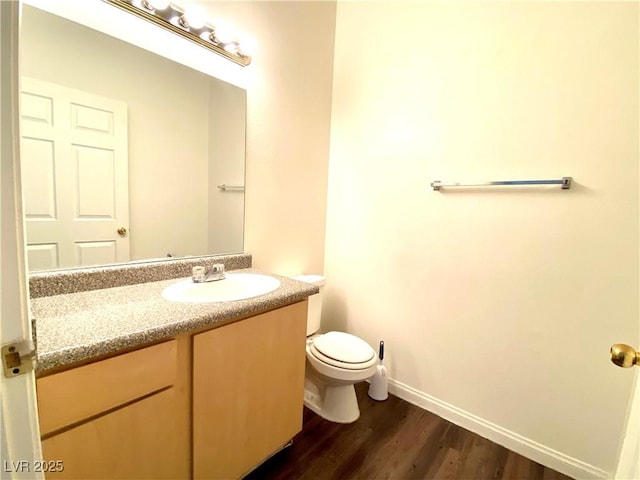 half bathroom with toilet, vanity, baseboards, and wood finished floors