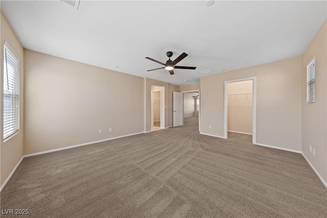 unfurnished bedroom featuring visible vents, a walk in closet, baseboards, carpet floors, and a ceiling fan