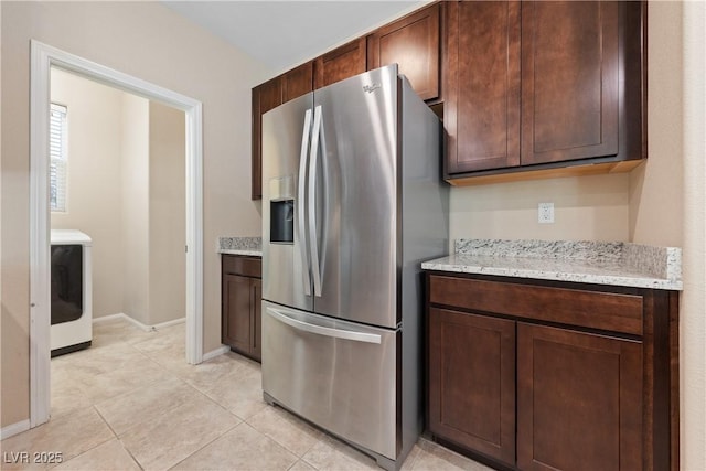 kitchen with baseboards, light stone counters, washer / dryer, stainless steel refrigerator with ice dispenser, and light tile patterned flooring