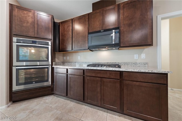 kitchen with dark brown cabinetry, light tile patterned flooring, stainless steel appliances, and light stone countertops