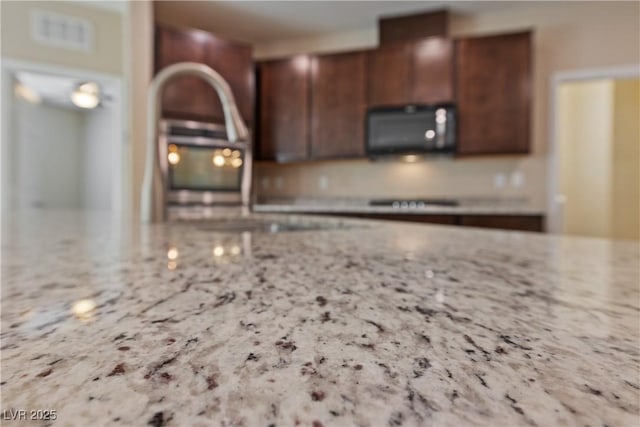 kitchen with light stone counters, visible vents, stovetop, a sink, and black microwave