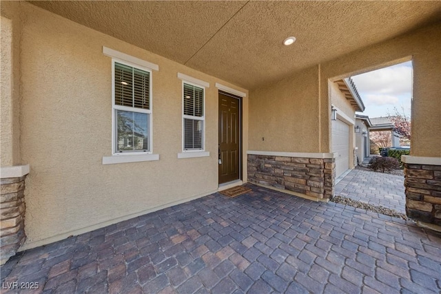 doorway to property with an attached garage, stone siding, and stucco siding