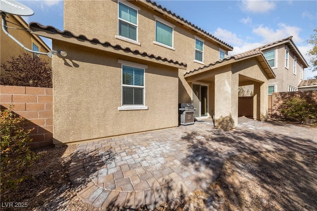 rear view of house with fence, a tile roof, stucco siding, a patio area, and an outdoor kitchen