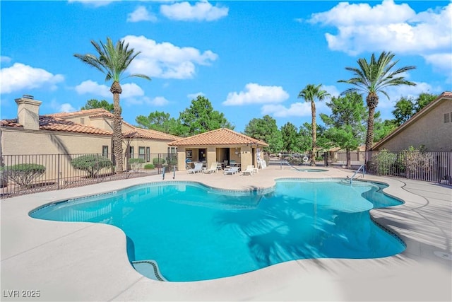 pool with a patio, fence, and a hot tub