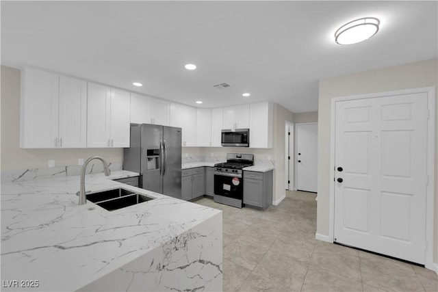 kitchen featuring gray cabinetry, light stone counters, recessed lighting, stainless steel appliances, and a sink