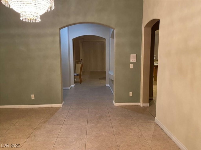 hallway with arched walkways, an inviting chandelier, baseboards, and light tile patterned flooring