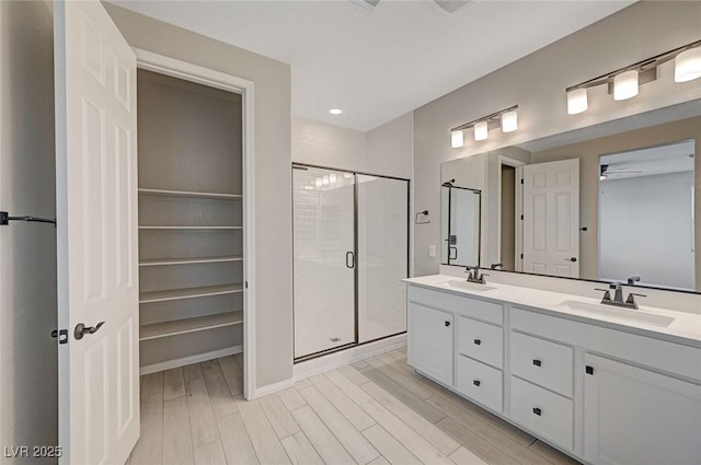 full bathroom with a sink, wood finished floors, a stall shower, and double vanity