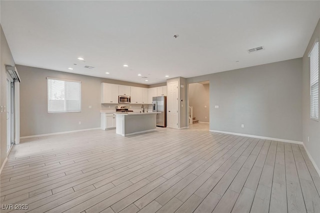 interior space featuring baseboards, visible vents, light wood finished floors, recessed lighting, and a sink