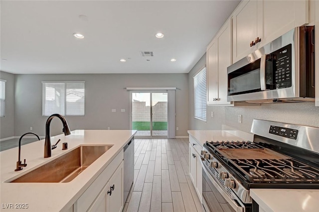 kitchen featuring visible vents, a sink, tasteful backsplash, light wood-style floors, and appliances with stainless steel finishes