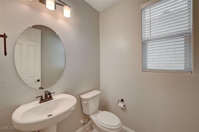 half bathroom with toilet, baseboards, and a sink