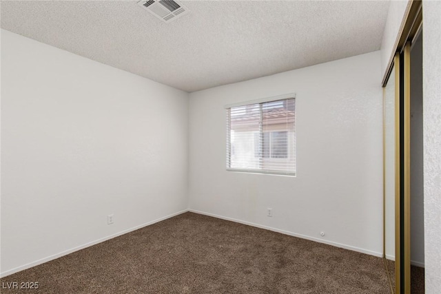 unfurnished bedroom with visible vents, baseboards, a closet, a textured ceiling, and dark colored carpet