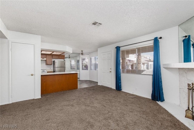 unfurnished living room with a textured ceiling, a fireplace, dark carpet, and ceiling fan