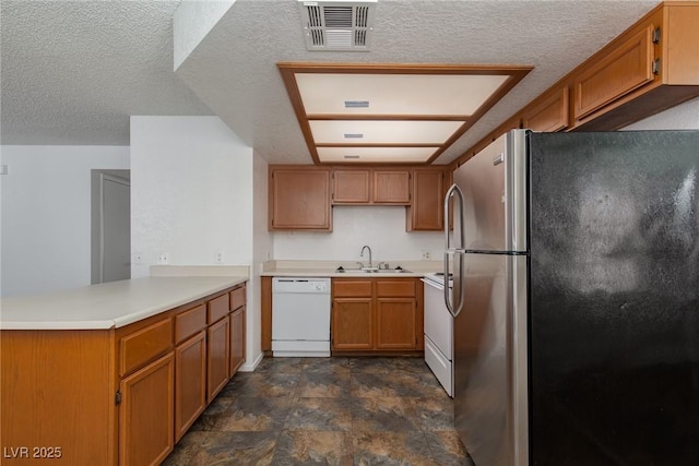 kitchen with visible vents, a sink, white appliances, a peninsula, and brown cabinetry