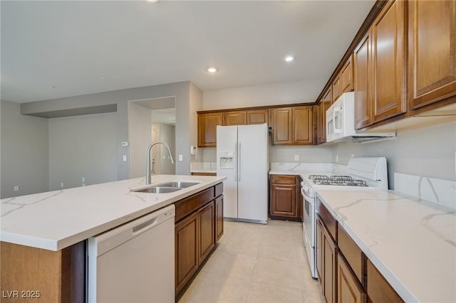 8348 Mokena Ave, Las Vegas, NV 89178 - kitchen featuring white appliances, a sink, brown cabinetry, an island with sink, and light stone counters