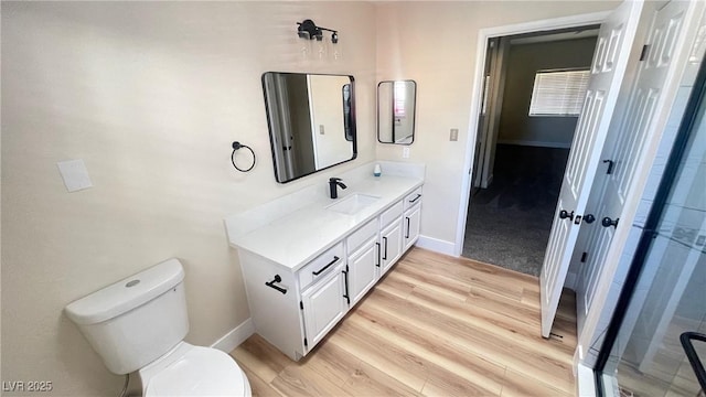 bathroom featuring baseboards, toilet, wood finished floors, an enclosed shower, and vanity