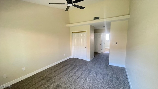 spare room featuring visible vents, baseboards, dark carpet, a towering ceiling, and a ceiling fan