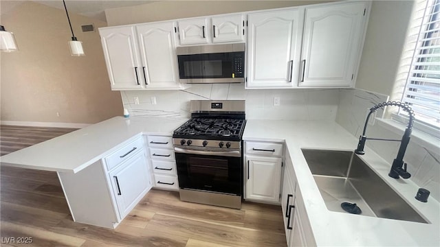 kitchen featuring appliances with stainless steel finishes, a peninsula, light wood-style floors, white cabinets, and a sink