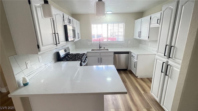 kitchen with light wood-type flooring, a sink, backsplash, stainless steel appliances, and a peninsula