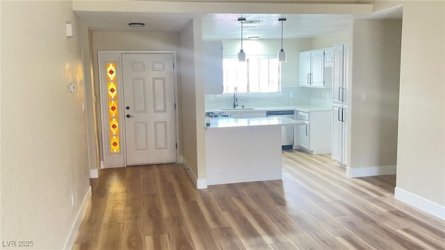 kitchen with light countertops, a peninsula, light wood-style floors, white cabinetry, and stainless steel dishwasher