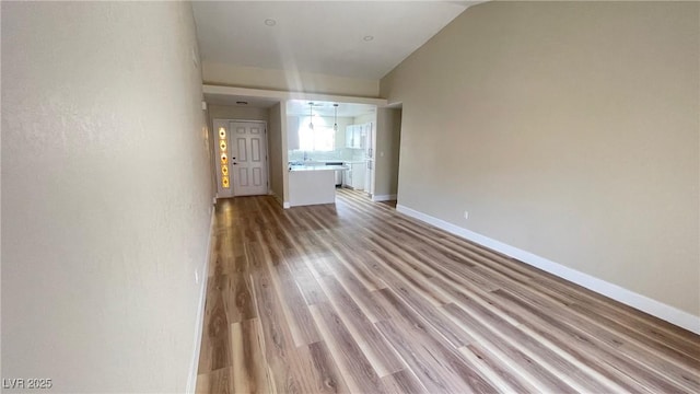 unfurnished living room featuring baseboards, vaulted ceiling, and light wood finished floors