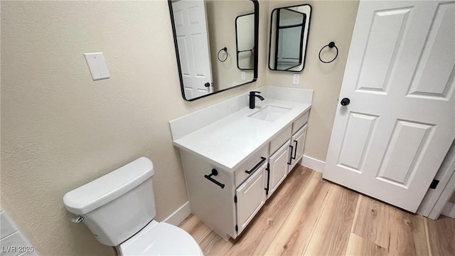 half bath with toilet, vanity, baseboards, and wood finished floors