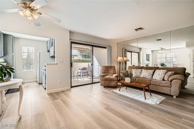 living room featuring light wood-type flooring, visible vents, baseboards, and a ceiling fan