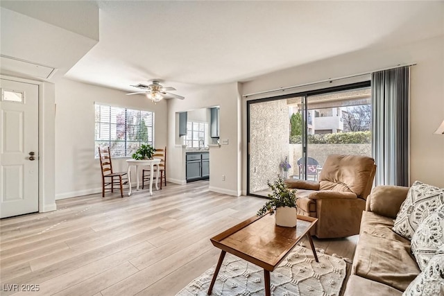 living area with light wood finished floors, a ceiling fan, and baseboards