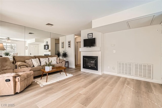 living room with light wood finished floors, visible vents, and a glass covered fireplace