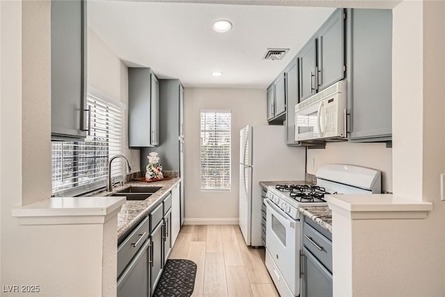 kitchen with white appliances, visible vents, gray cabinets, a sink, and light wood-style floors