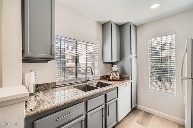 kitchen with white appliances, baseboards, gray cabinets, a sink, and light wood-type flooring