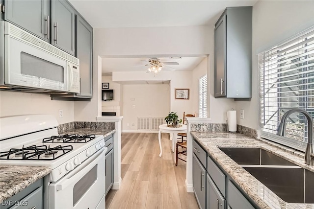 kitchen featuring visible vents, gray cabinets, a sink, light stone counters, and white appliances